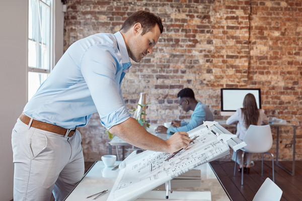 Architekt, der einen Plan auf einem Zeichentisch für ein Projekt oder eine Entwicklung in seinem Büro zeichnet.