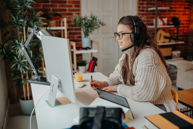 Frau mit Kopfhörern am Laptop im Home-Office