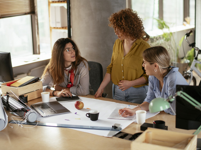 Drei Frauen planen oder disktuieren am Schreibtisch über das Projekt/die Arbeit