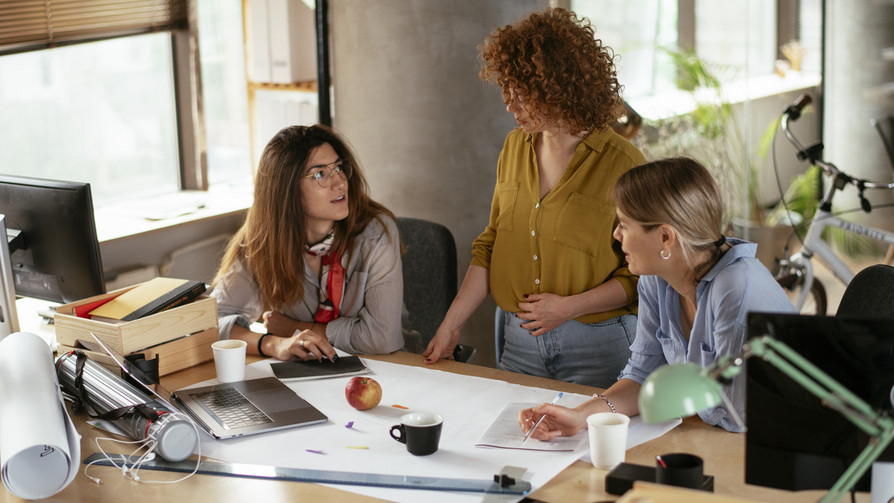 Drei Frauen planen oder disktuieren am Schreibtisch über das Projekt/die Arbeit