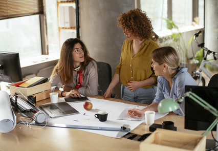 Drei Frauen planen oder disktuieren am Schreibtisch über das Projekt/die Arbeit