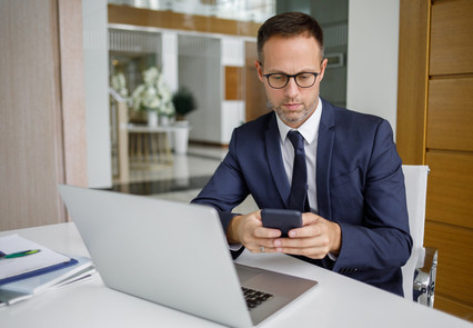 Mann mit Anzug und Smartphone in der Hand am Schreibtisch