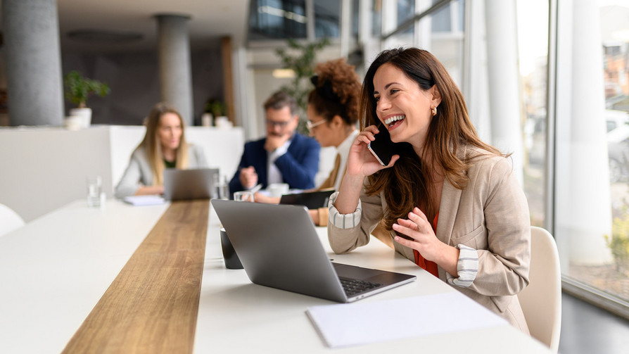 Mitarbeiterin telefoniert am Tisch mit Laptop