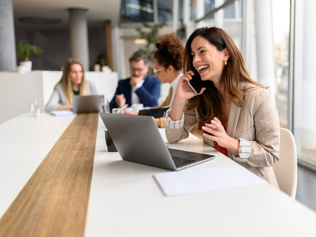 Mitarbeiterin telefoniert am Tisch mit Laptop